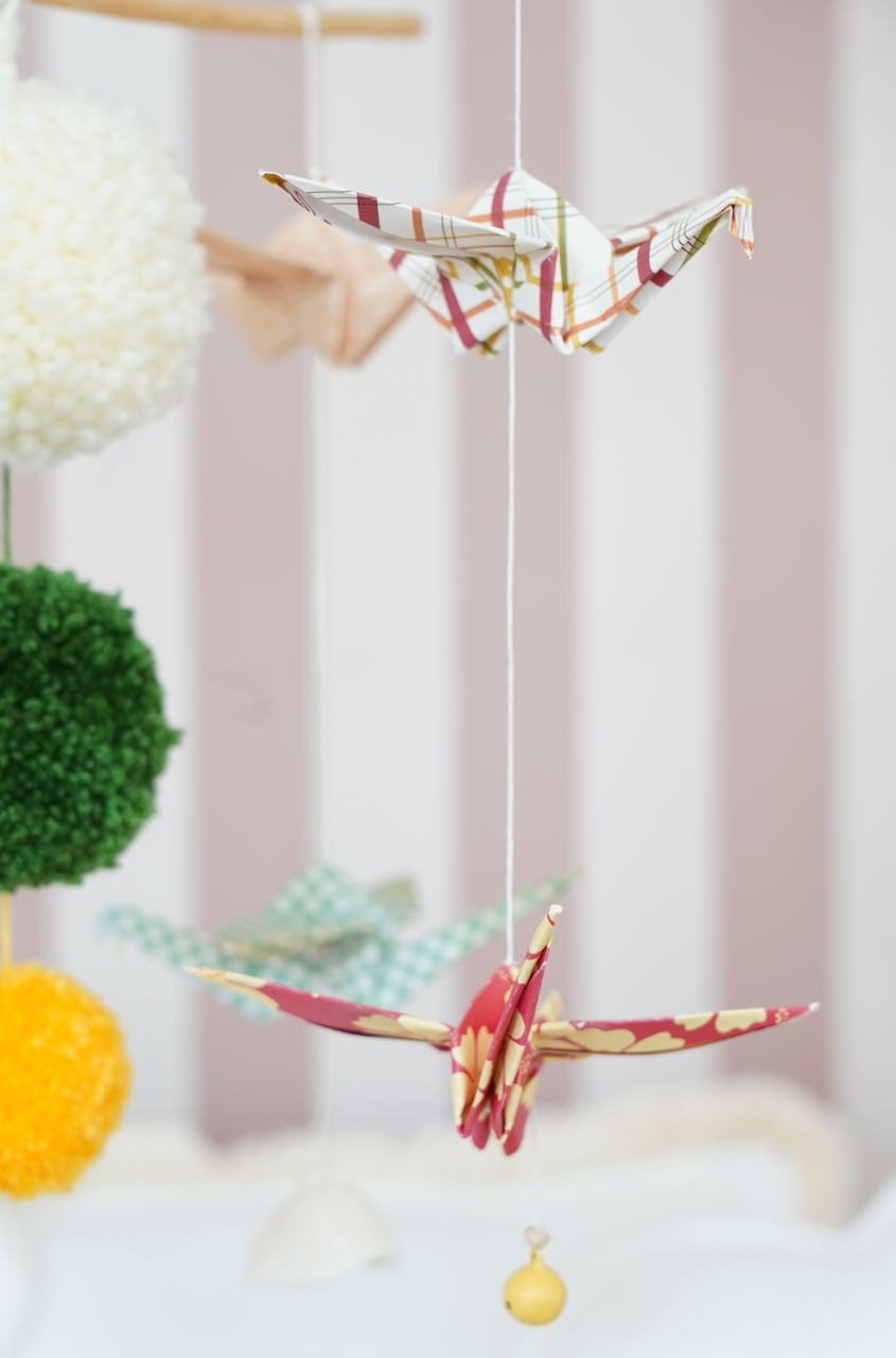 3. Close-up of origami cranes and colorful yarn pompoms on a nursery mobile, highlighting paper texture and intricate design