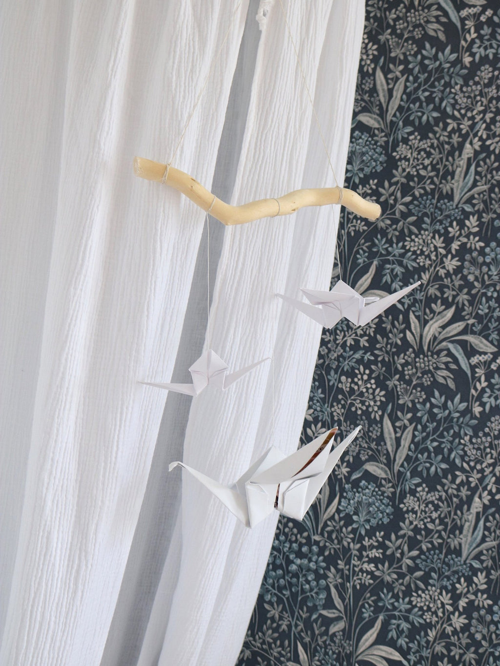 3. White origami nursery mobile with paper cranes and wooden stick against floral wallpaper