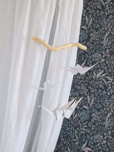 3. White origami nursery mobile with paper cranes and wooden stick against floral wallpaper