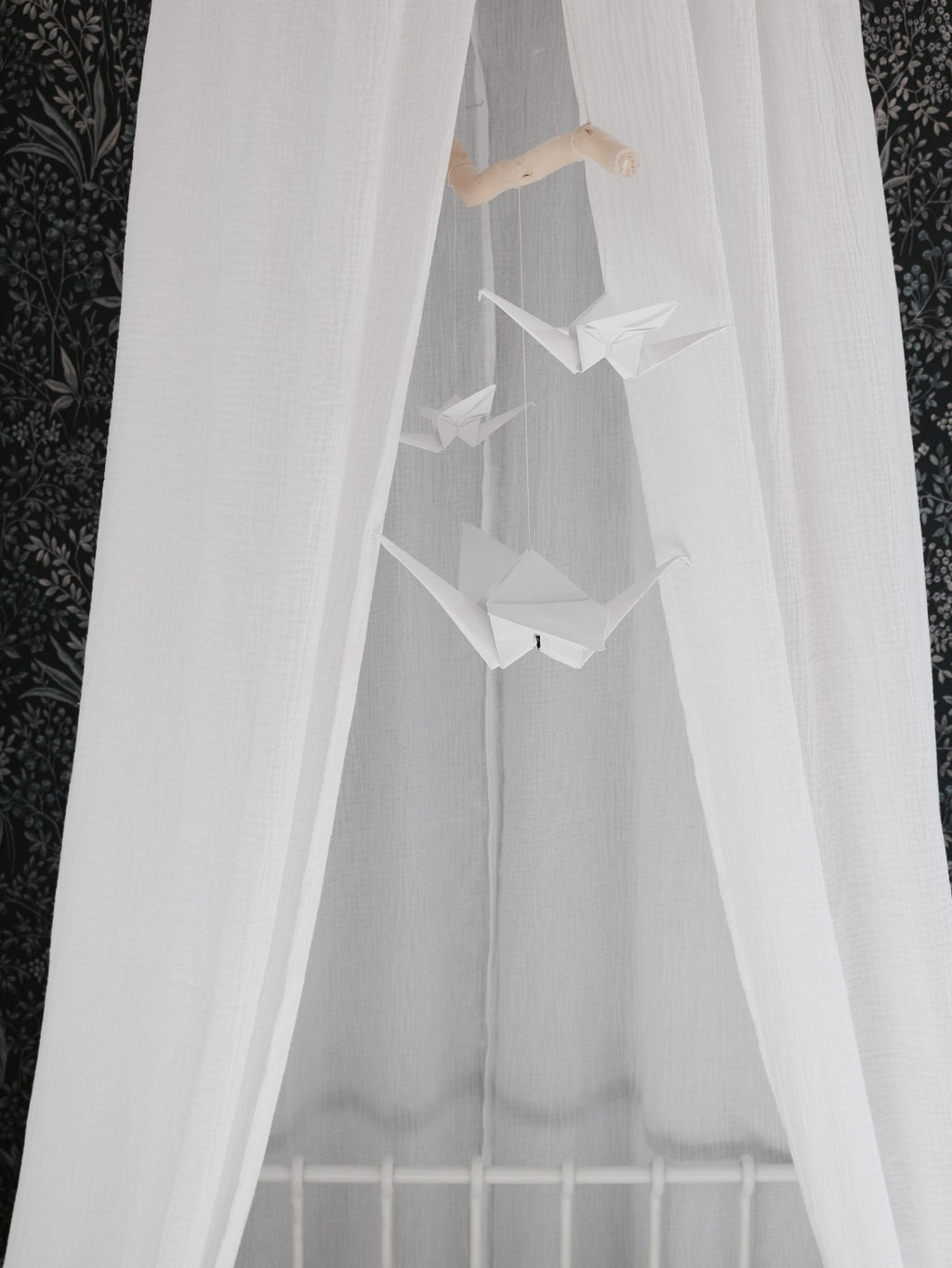 1. White origami nursery mobile with paper cranes hanging in front of sheer white curtains in a cozy room setting
