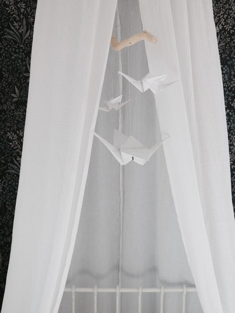 1. White origami nursery mobile with paper cranes hanging in front of sheer white curtains in a cozy room setting