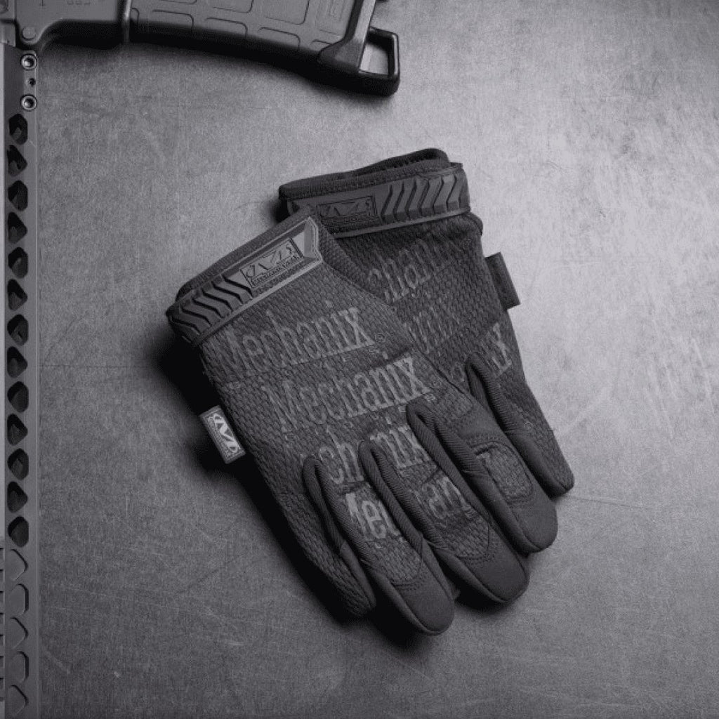 1. Pair of black Mechanix tactical gloves on textured surface next to firearm