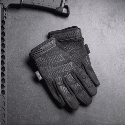 1. Pair of black Mechanix tactical gloves on textured surface next to firearm