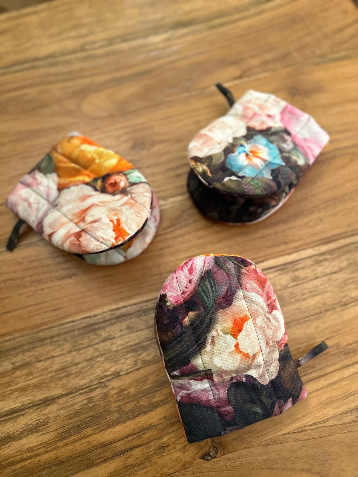 2. Three floral printed oven gloves with double wool filling arranged on wooden table, highlighting variety and style