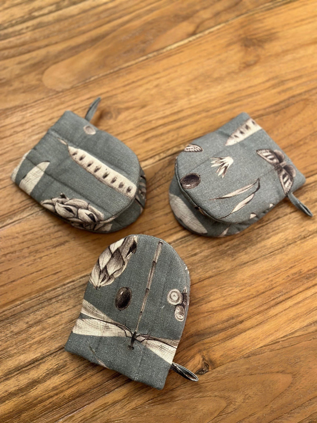 2. Three Hortensias Home oven gloves in seeds aqua print with double wool filling arranged on wooden surface