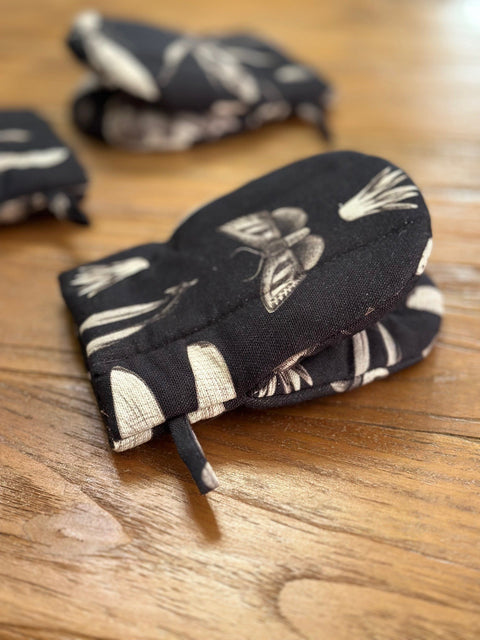 1. Black oven glove with white botanical print, featuring double wool filling, placed on wooden surface