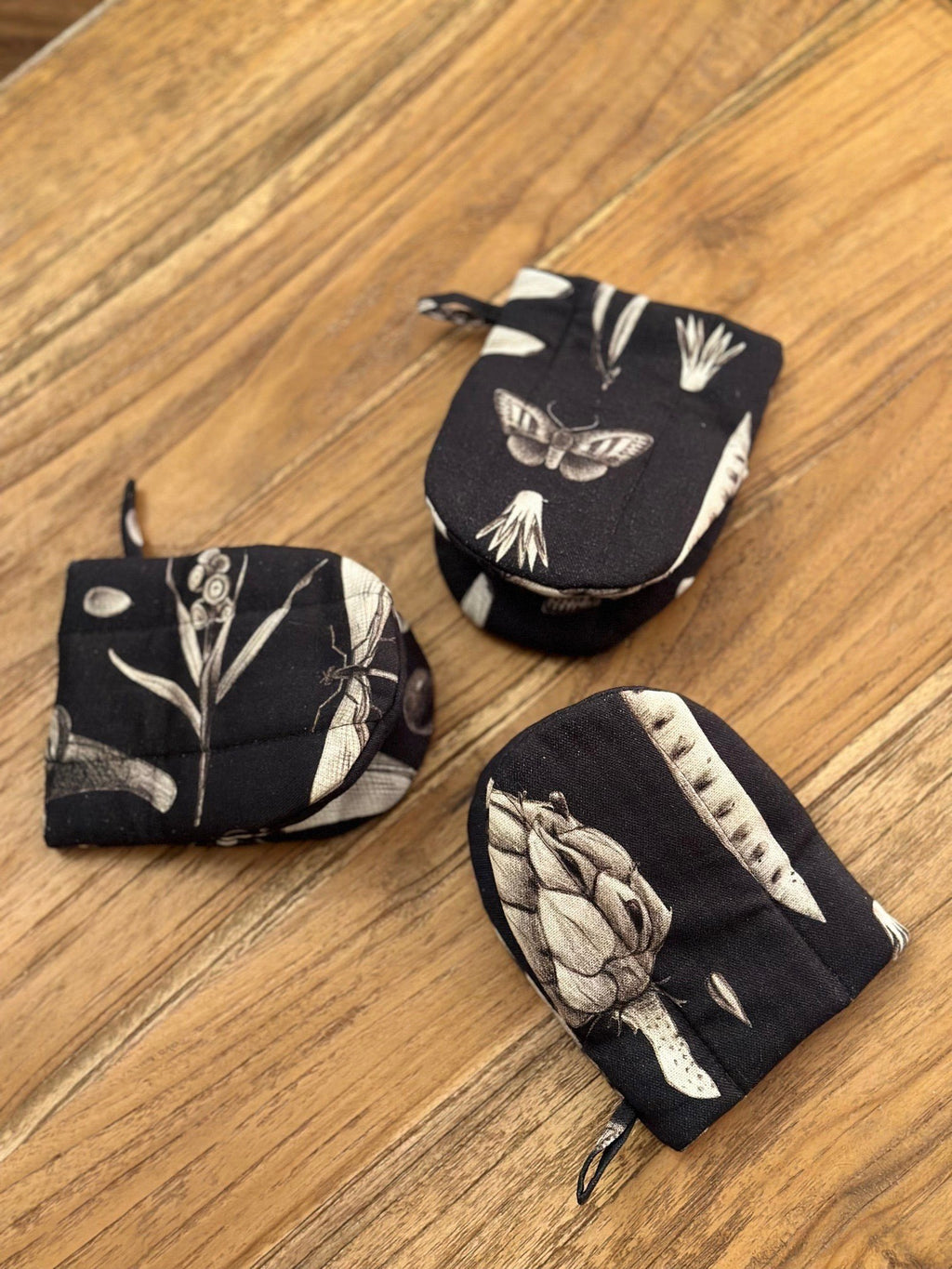 2. Three black oven gloves with white botanical print, arranged on wooden surface