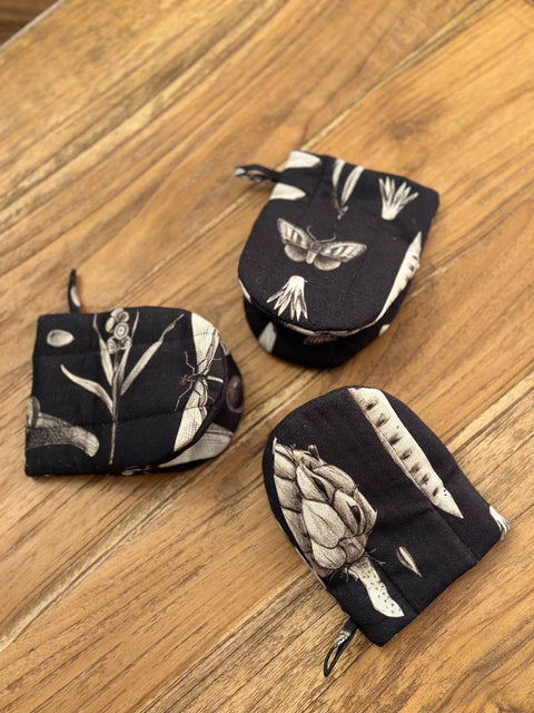 2. Three black oven gloves with white botanical print, arranged on wooden surface