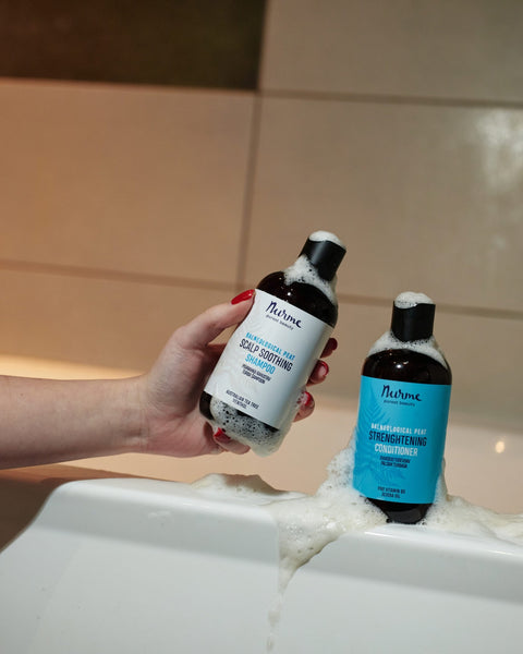 1. Hand holding Nurme Palneological Peat Scalp Soothing Shampoo and Strengthening Conditioner bottles with foam in bathroom setting