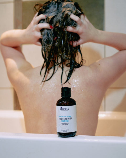 1. Person washing hair in bathtub with Nurme Palneological Peat Scalp Soothing Shampoo bottle in foreground