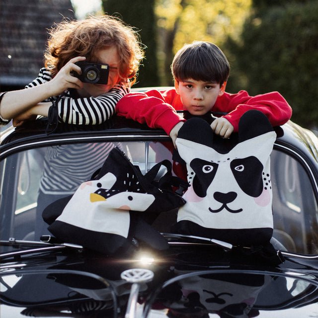 3. Kids with Muni Panda and Penguin backpacks on a car, highlighting outdoor adventure theme