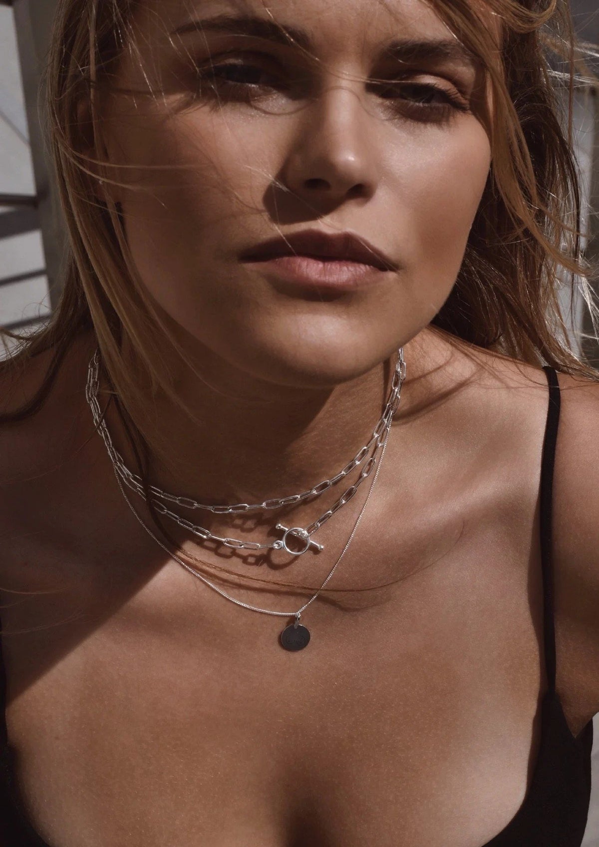 2. Close-up of woman wearing NO MORE silver paper clip choker, layered with other necklaces, in outdoor setting