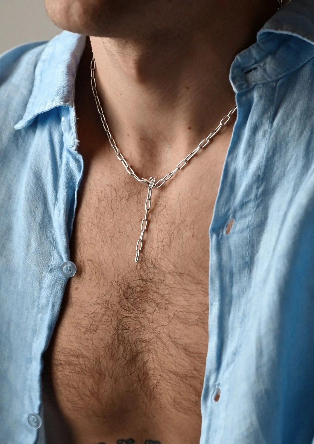 12. Man wearing silver Y-shaped necklace with blue button-up shirt
