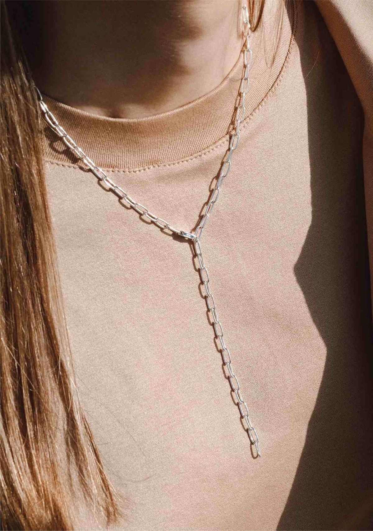 6. Woman wearing silver Y-shaped necklace over beige top in natural light