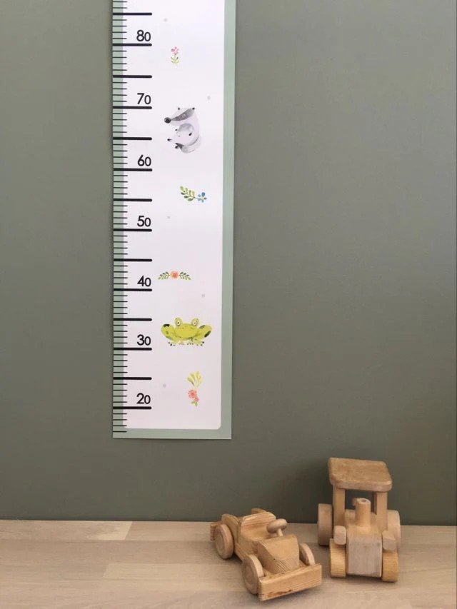 1. Children's paper growth chart with playful animal illustrations on a green wall, featuring a wooden toy car and truck at the base
