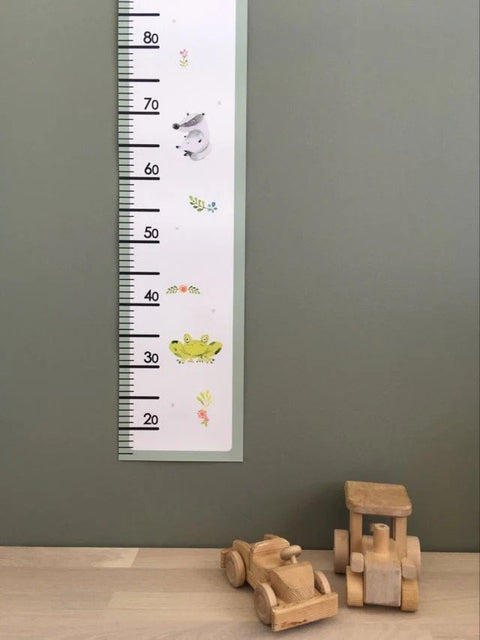 1. Children's paper growth chart with playful animal illustrations on a green wall, featuring a wooden toy car and truck at the base
