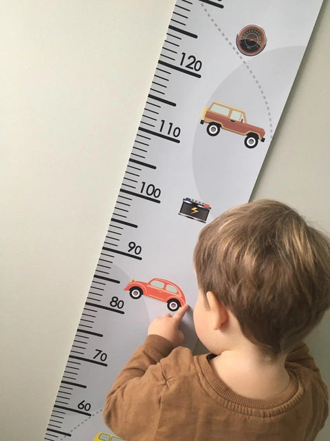3. Child pointing at retro cars-themed paper growth chart on wall, featuring colorful car illustrations and measurement scale, in a child's room setting