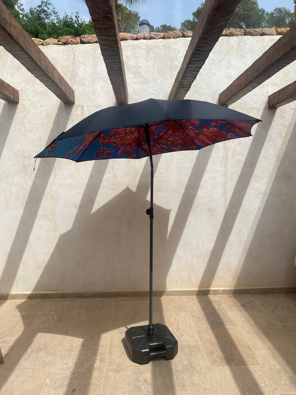 1. HAPPYSWEEDS parasol with black base on sunlit terrace, featuring floral print canopy and wooden beams overhead