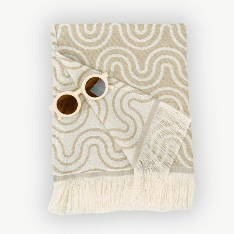 2. Flat lay of beige Patulove bamboo towel for kids with white fringe and floral sunglasses on top