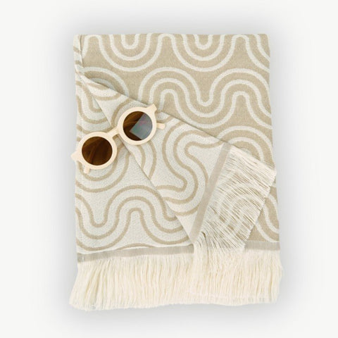 2. Flat lay of beige Patulove bamboo towel for kids with white fringe and floral sunglasses on top