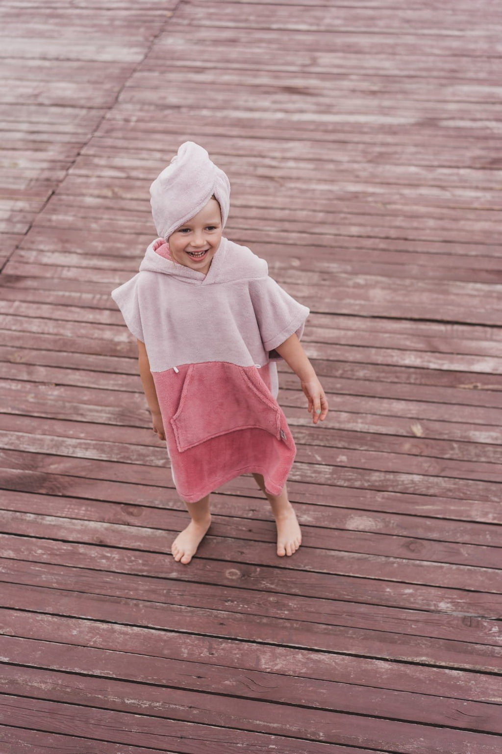 5. Child in pink bath poncho and hair turban standing on wooden deck