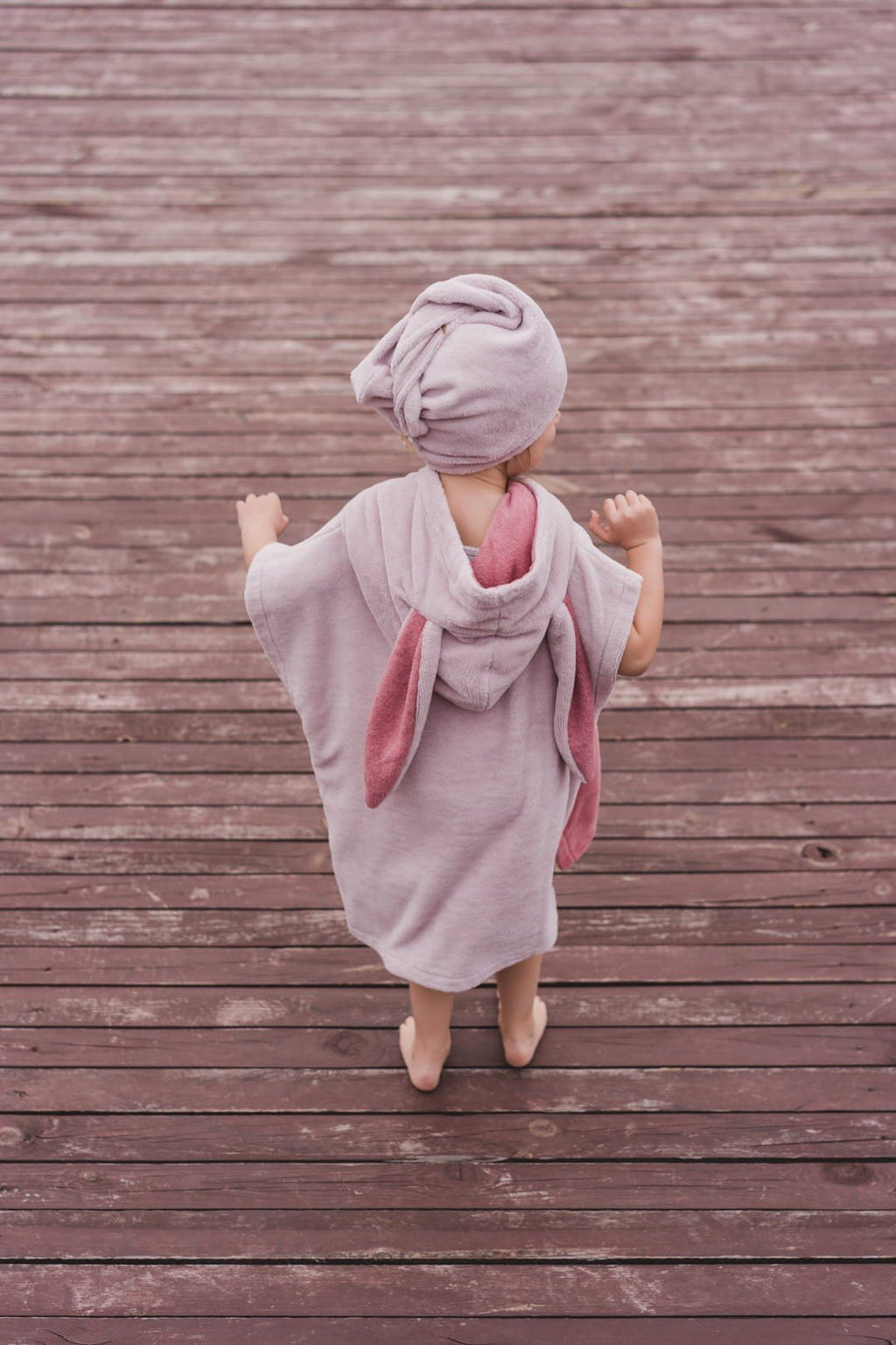 6. Back view of child in pink bath poncho and hair turban on wooden deck
