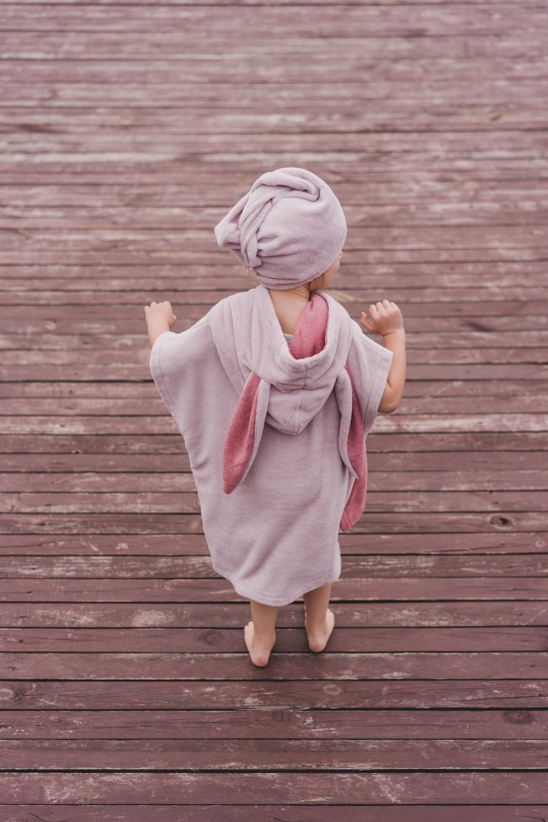 6. Back view of child in pink bath poncho and hair turban on wooden deck