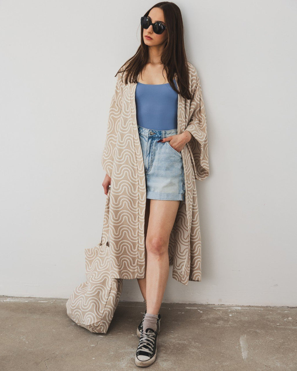 5. Woman wearing Patulove sand kimono with blue top, denim shorts, and sneakers, holding matching bag