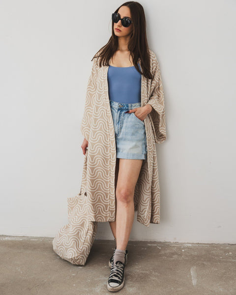 5. Woman wearing Patulove sand kimono with blue top, denim shorts, and sneakers, holding matching bag