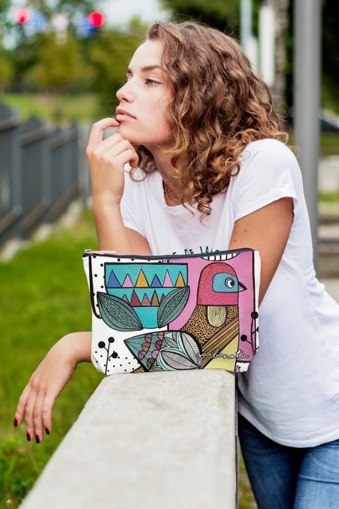 4. Woman posing with Garbanota Little Bird makeup pouch, showcasing colorful design and relaxed outdoor setting