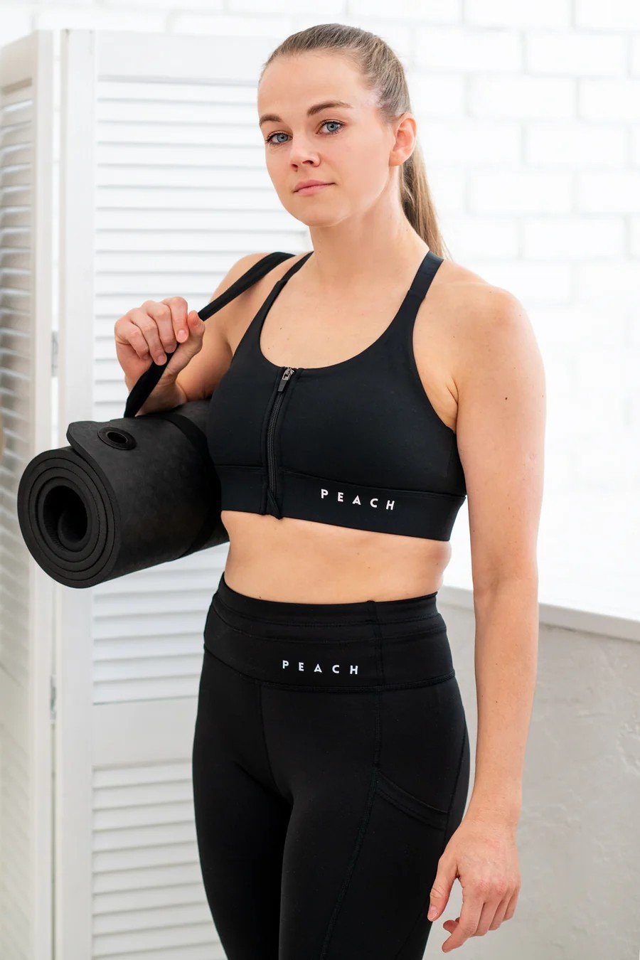 2. Woman holding yoga mat in Peachlabel PocketPerfect Inky Black leggings, highlighting high waist and side pockets