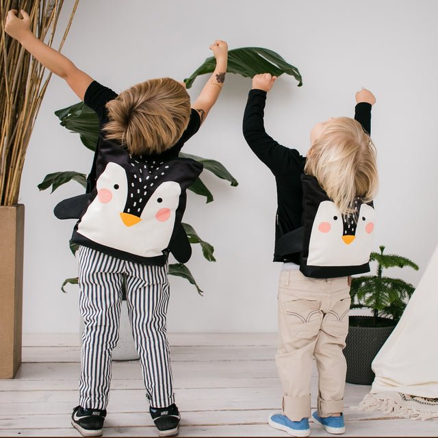 1. Two children wearing Muni Penguin backpacks in a playful indoor setting