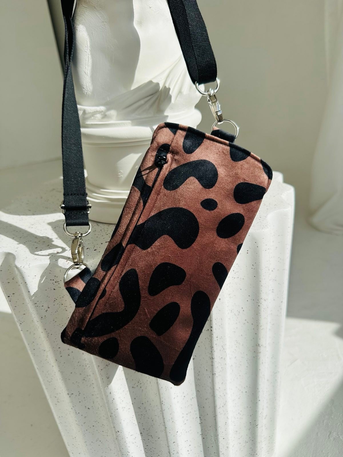 2. Garbanota classic leopard velour phone bag with adjustable strap displayed on white pedestal in studio setting