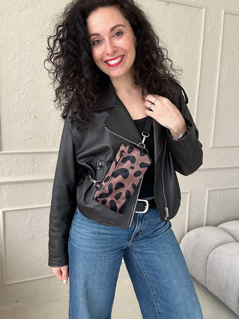 1. Woman wearing Garbanota classic leopard velour phone bag with adjustable strap, styled with black leather jacket and jeans