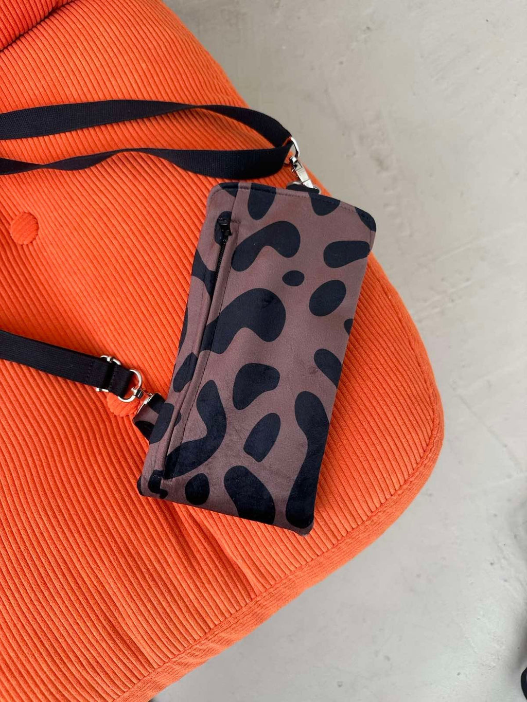 3. Close-up of Garbanota classic leopard velour phone bag on orange textured surface, showing front zippered pocket