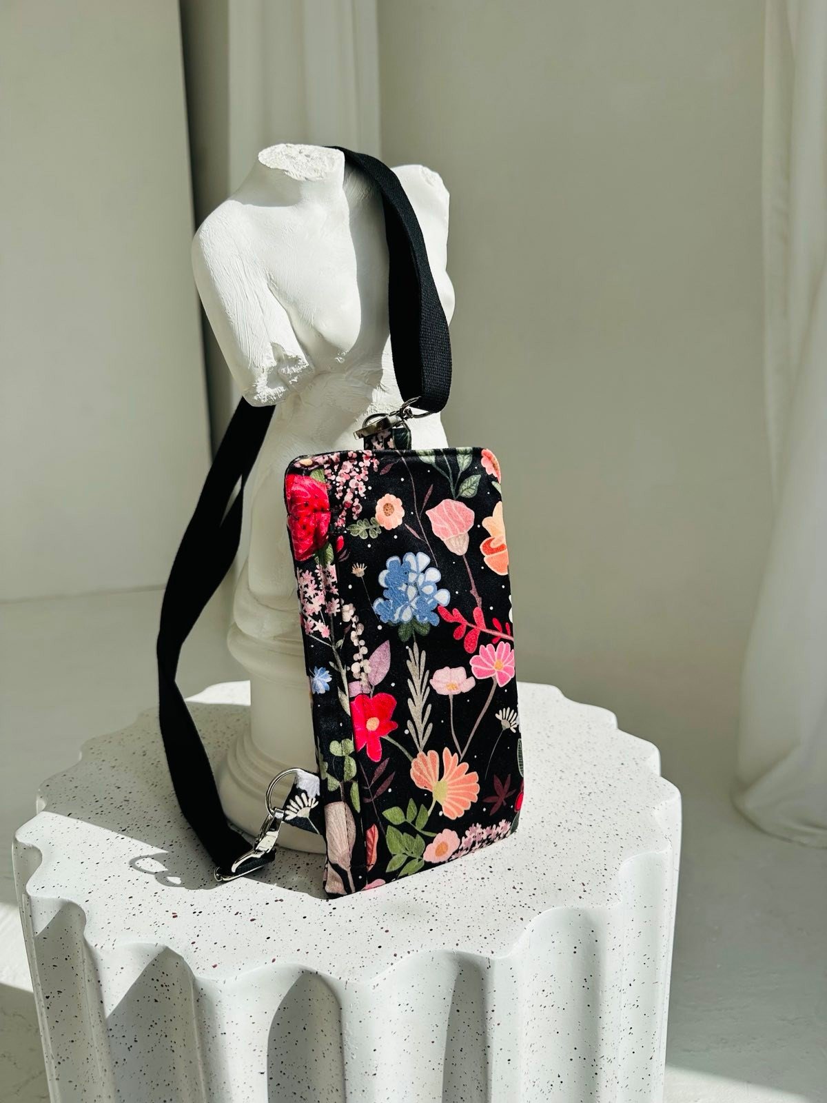 3. Studio shot of Garbanota Curly Summer Night phone bag with floral design, displayed on white sculpture
