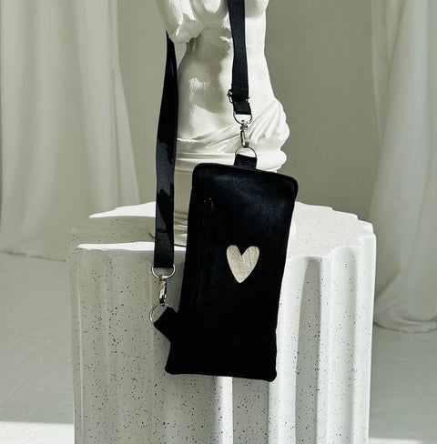 2. Black velour phone bag with heart design by Garbanota, displayed on a white pedestal with adjustable strap
