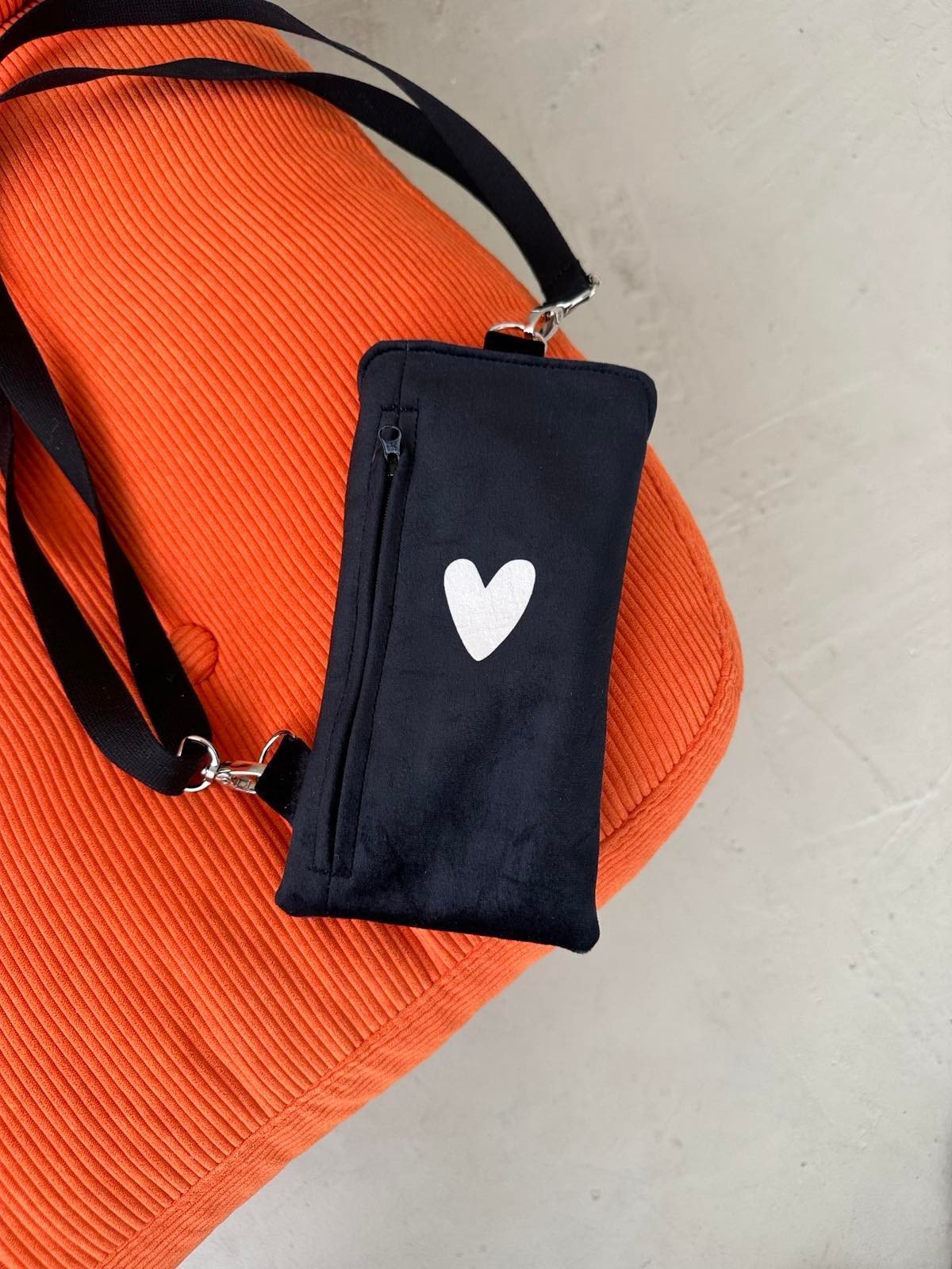 3. Black velour phone bag with heart design by Garbanota, shown on an orange chair with adjustable strap