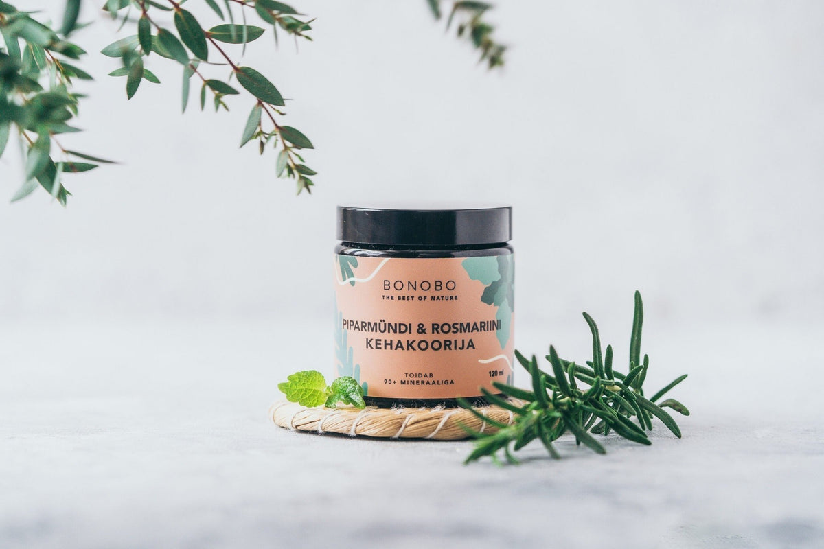 2. BONOBO Peppermint & Rosemary body scrub jar on a woven mat with rosemary and mint leaves
