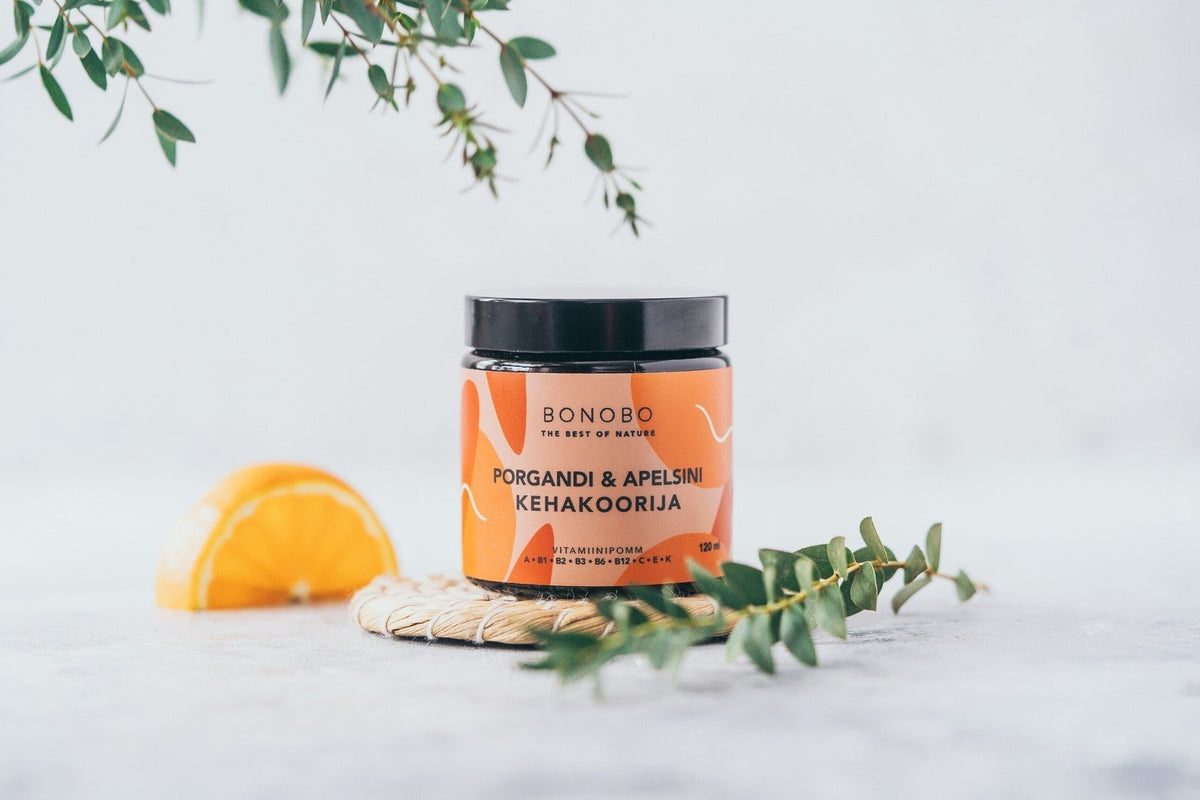 2. BONOBO Orange & Carrot body scrub jar on a woven mat with orange slice and greenery