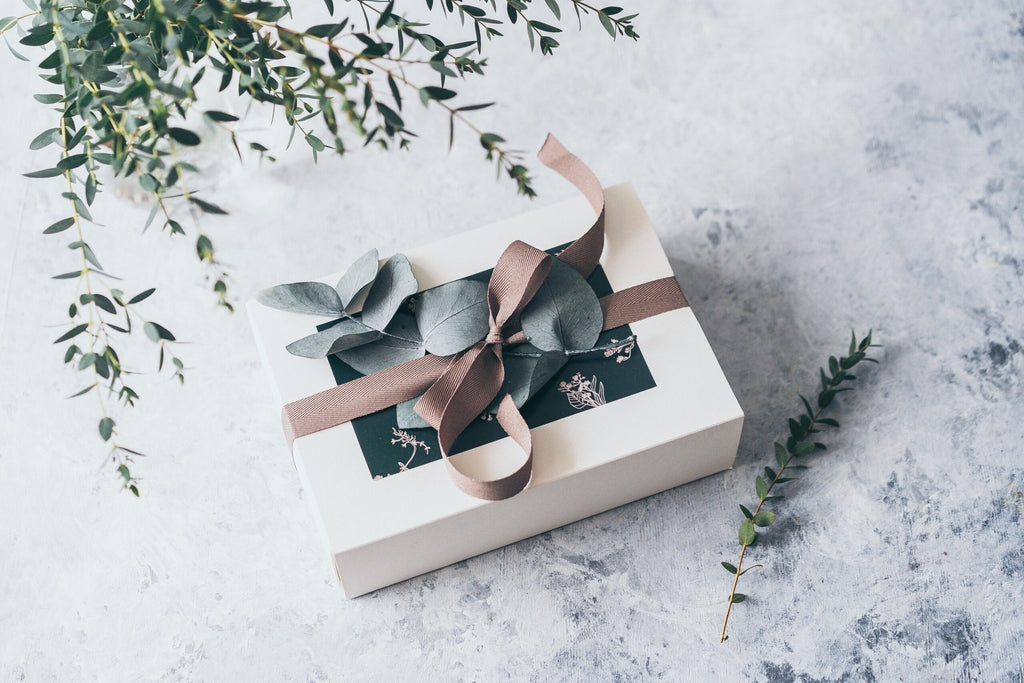4. BONOBO Piece of Heaven gift box with ribbon and eucalyptus leaves on a textured surface with greenery