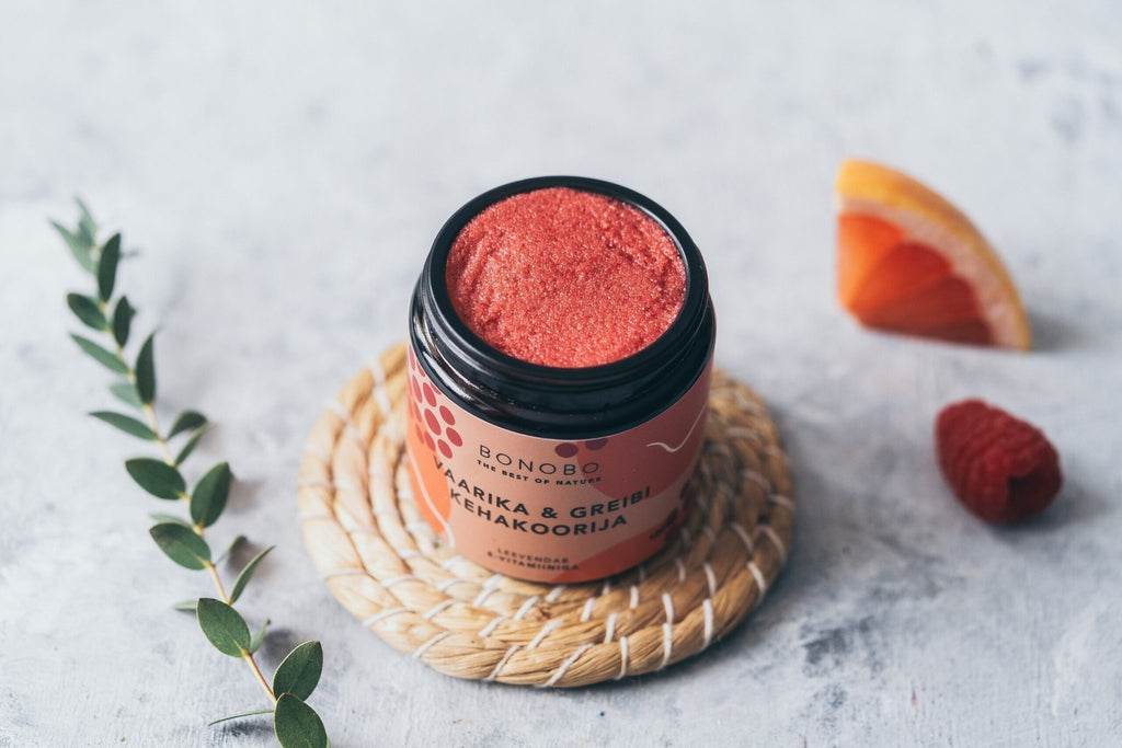 3. Open jar of BONOBO Raspberry & Grapefruit body scrub on a woven mat with raspberry and grapefruit slice