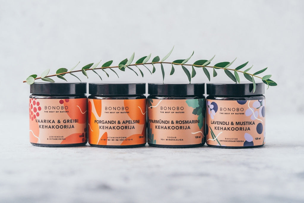 2. Four BONOBO body scrub jars lined up with greenery on a textured surface