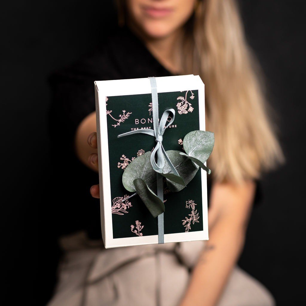 1. Woman holding BONOBO Piece of Heaven gift box with floral design and ribbon against a dark background