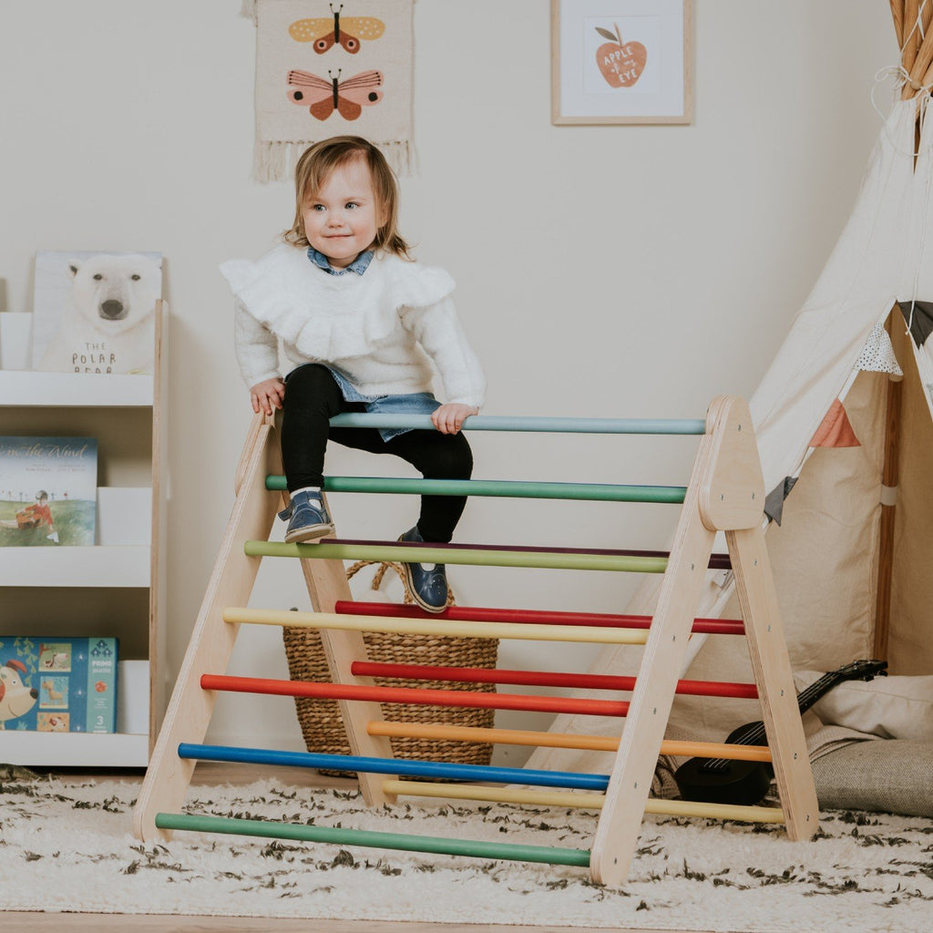 1. Child sitting on leg&go Pikler Triangle with rainbow bars in cozy playroom setting