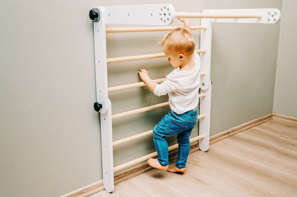 7. Toddler climbing a white Pikler triangle used as a Swedish wall in a room with wooden flooring