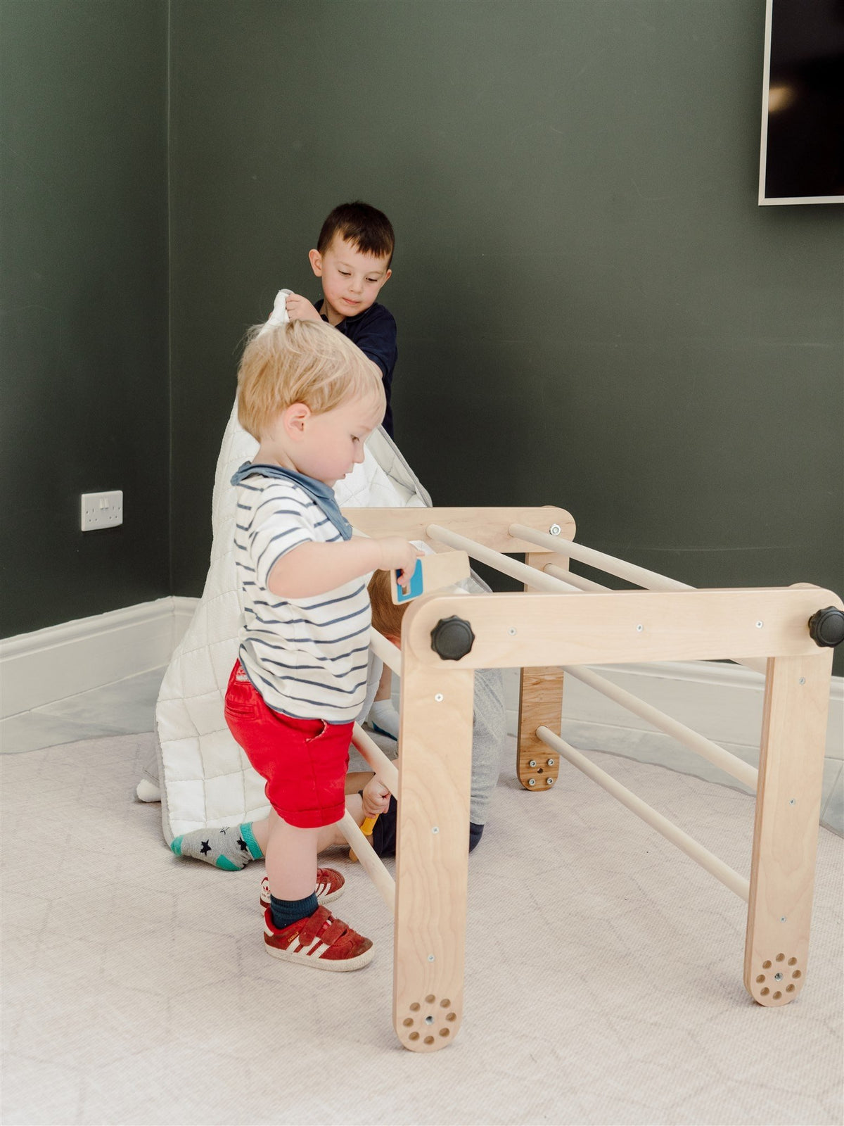2. Two young children interacting with a wooden Pikler triangle in a room with dark walls