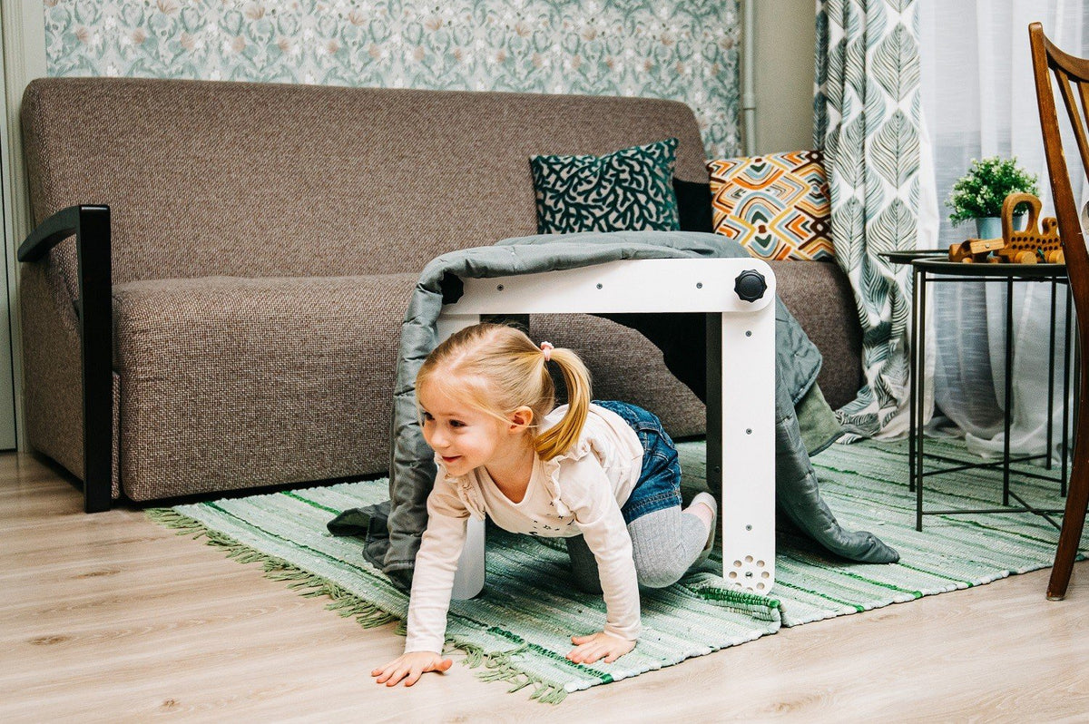 6. Girl crawling under a white Pikler triangle covered with a blanket in a living room