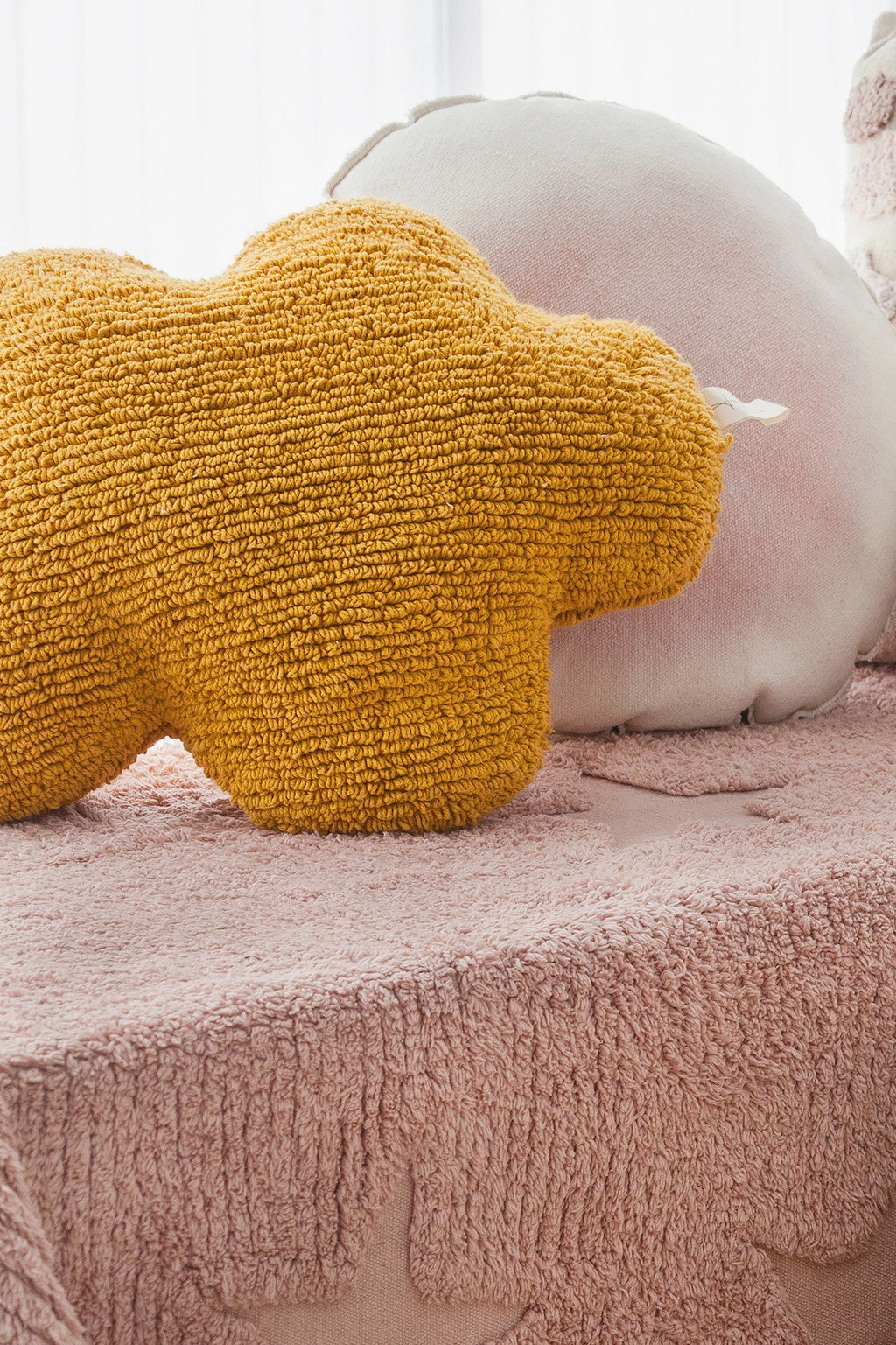 1. Mustard cloud-shaped pillow on pink textured bedspread with other pillows in a cozy setting