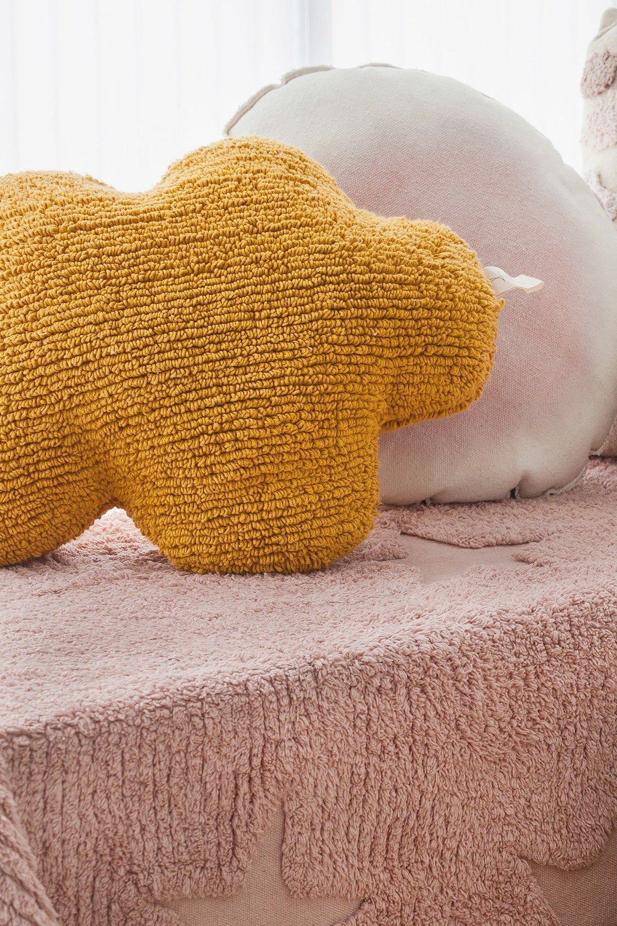 1. Mustard cloud-shaped pillow on pink textured bedspread with other pillows in a cozy setting